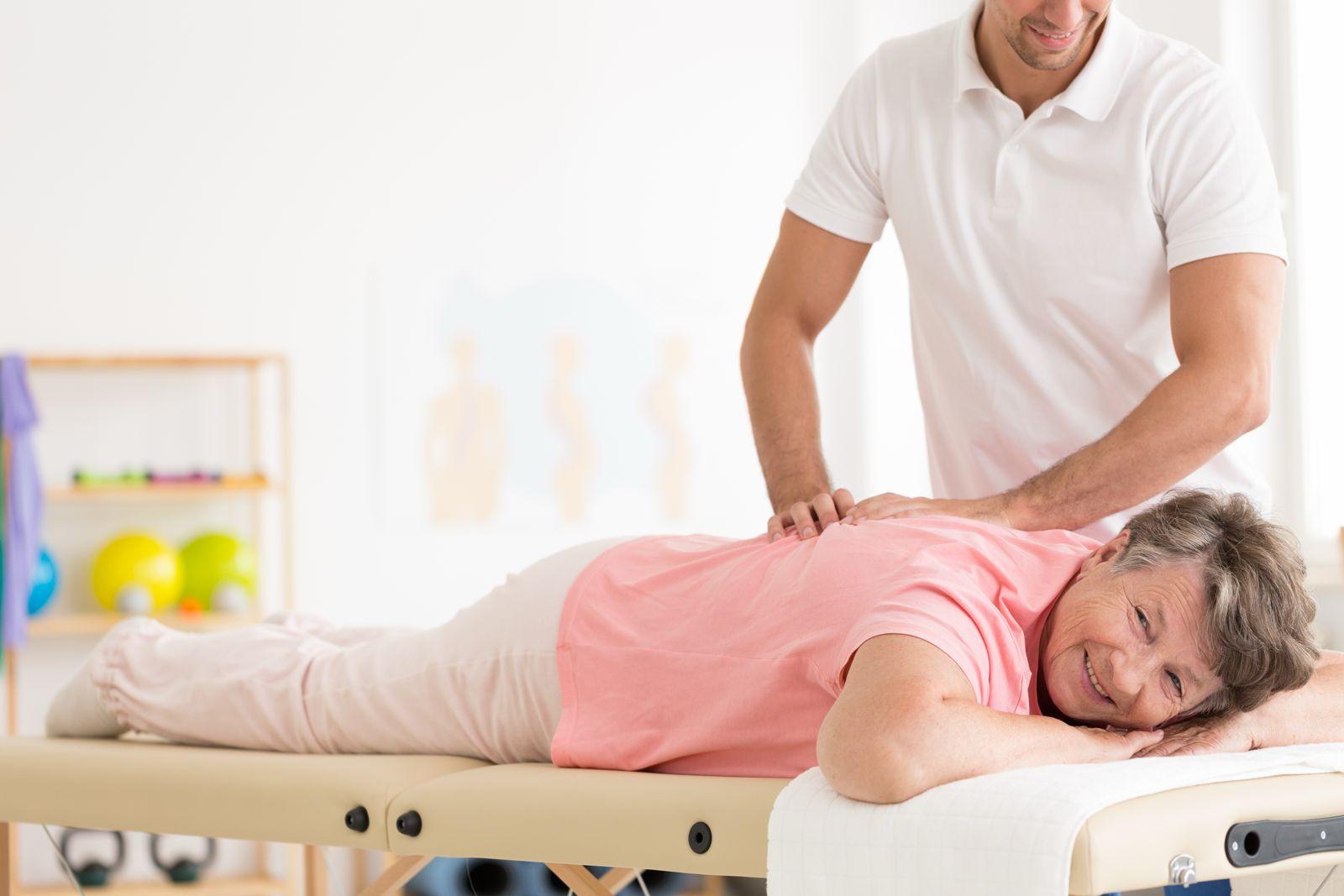 Chiropractor treating a smiling patient’s back on a treatment couch